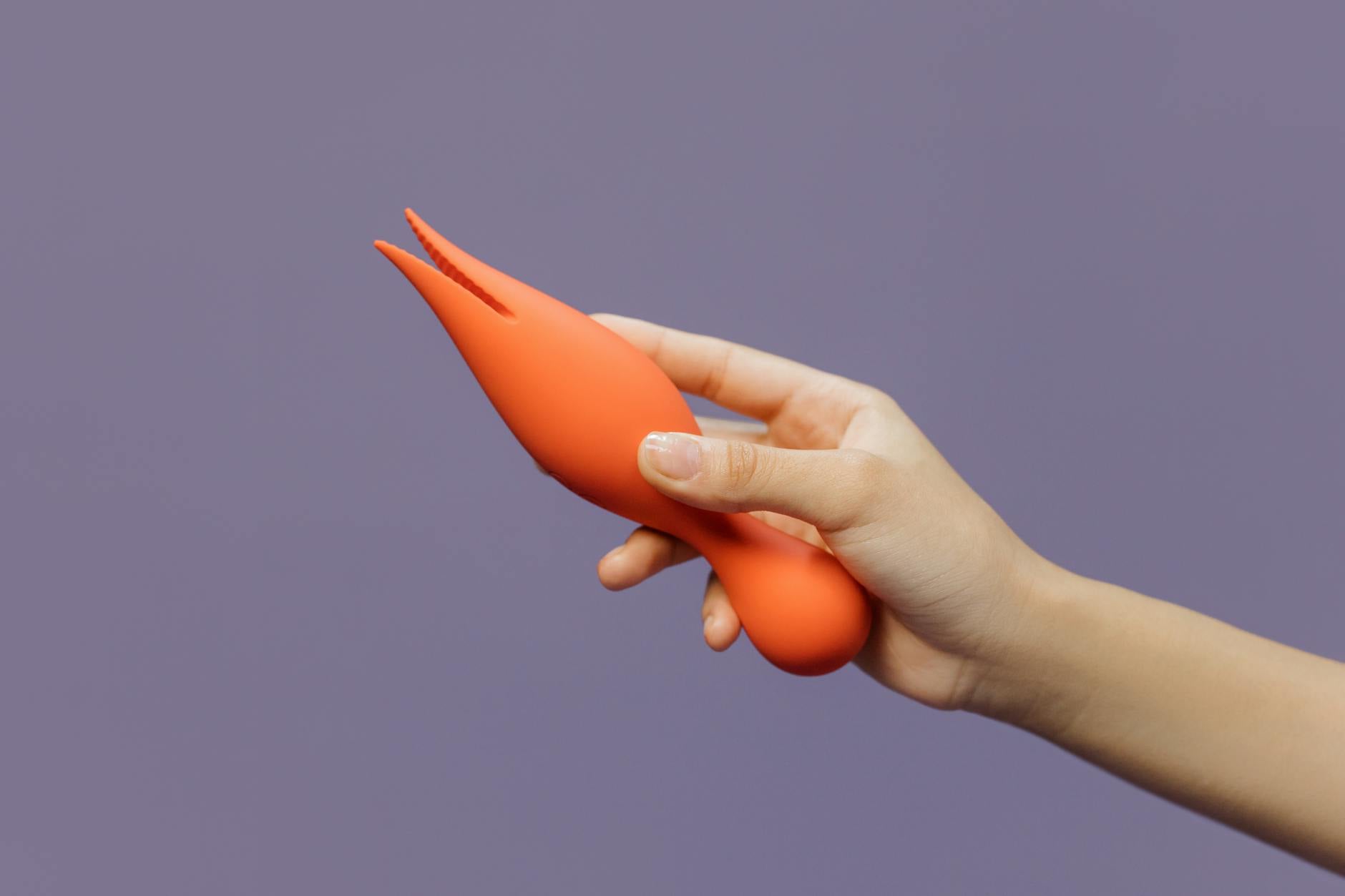 Close-up of a hand holding an orange vibrator, representing modern sensual exploration